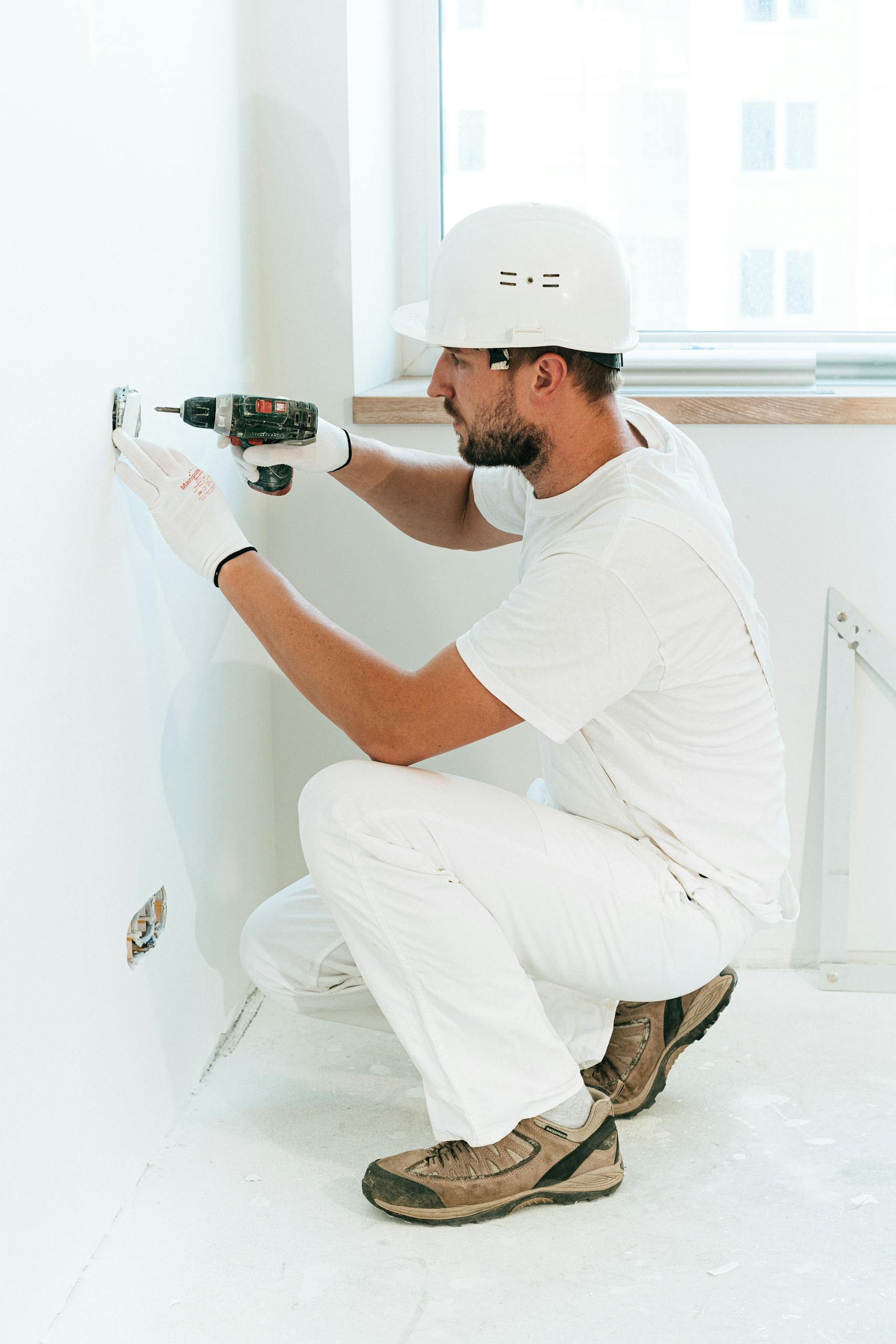 Electrician in dubai wearing a helmet uses a drill to install a wall outlet inside a dubai villa complex.